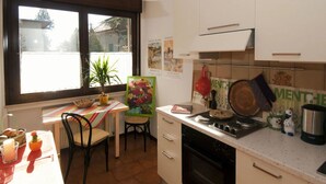Una cucina con una finestra, un tavolo da pranzo, sedie, un fornello e diversi utensili da cucina.