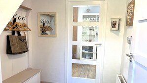 A hallway with a bench, a coat rack, a mirror, a door with a view into a room, and a radiator. - Holiday Home Near Beach (Ouddorp)