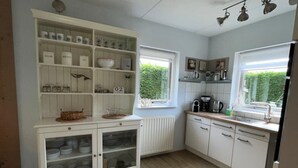 A kitchen with white cabinetry, a built-in shelf unit, a window, and a radiator. - Holiday Home Near Beach (Ouddorp)