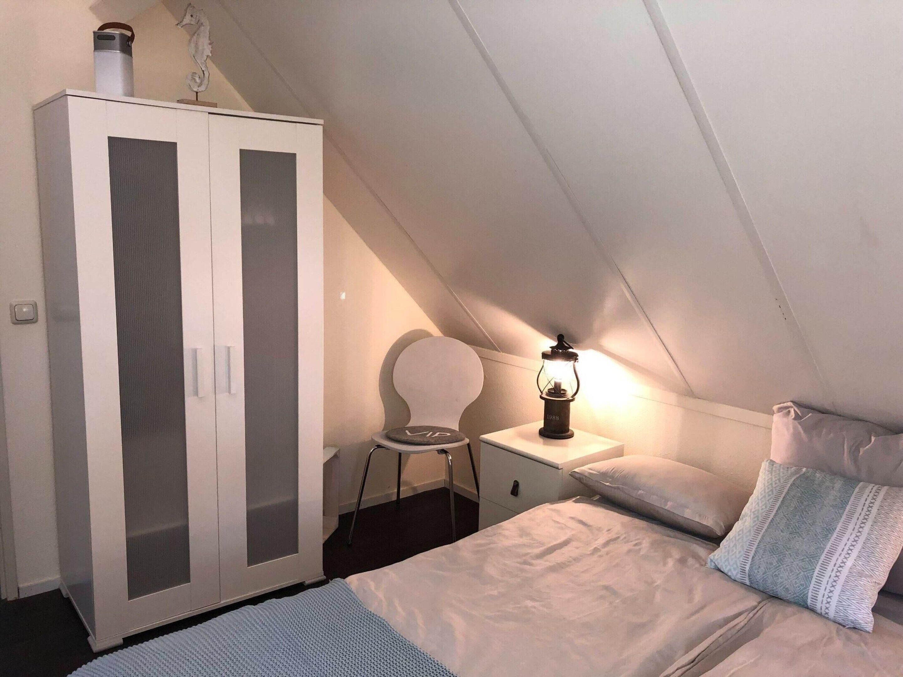 Quarto com cama, guarda-roupa, cadeira e mesa com candeeiro.