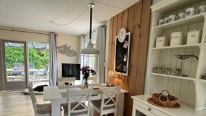 A dining area with a white table and chairs, a hanging light fixture, and a shelf with kitchenware. - Holiday Home Near Beach (Ouddorp)