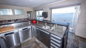 A modern kitchen with stainless steel appliances, a large island with a sink, and a view of the sea through a sliding door.