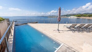 A swimming pool with a view of the sea, a beach, and lounge chairs.