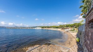 A coastal view with clear waters, a sandy beach, and a stone staircase leading down to the water.