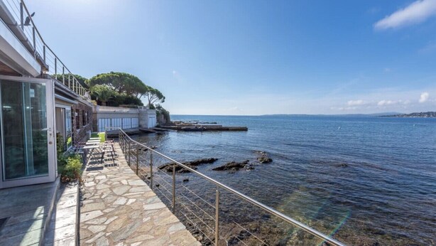 A coastal walkway with stone flooring, metal railings, and a view of the sea.