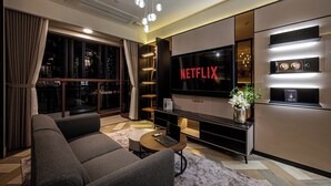 A modern living room with a large flat-screen TV, a sofa, a coffee table, and a bookshelf. - Metropole Apartment Thu Thiem (Ho Chi Minh City)