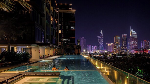 A swimming pool with a city skyline view at night. - Metropole Apartment Thu Thiem (Ho Chi Minh City)