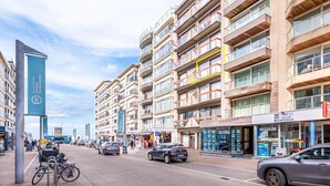Un immeuble à plusieurs étages doté de balcons, d’un support à vélos et de boutiques, dont une agence immobilière.