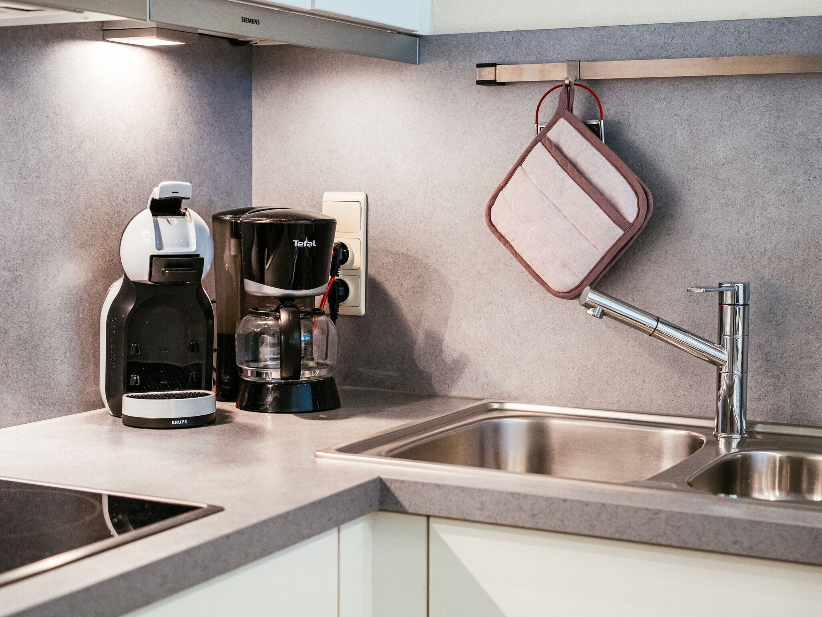 A modern kitchen with a coffee maker, a kettle, and a hanging pot rack.