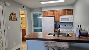 A compact kitchen with a central island, wooden cabinets, a microwave, and a refrigerator. - SB#3: Dog Friendly, Across from the Beach, Free Daily Activities! (Pensacola)