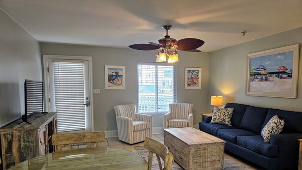 A living room with a glass-top table, striped armchairs, a blue sofa, and a ceiling fan. - SB#3: Dog Friendly, Across from the Beach, Free Daily Activities! (Pensacola)