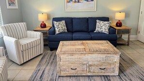 A living room with a blue sofa, striped armchair, wooden coffee table, and two side tables with lamps. - SB#3: Dog Friendly, Across from the Beach, Free Daily Activities! (Pensacola)