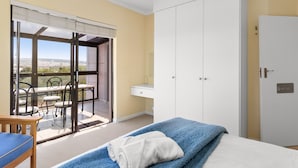 A bedroom with a bed, a desk, a chair, and a view of the outdoors.