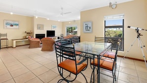 A spacious living area with a glass-top dining table, comfortable seating, a flat-screen TV, and a telescope on a tripod.