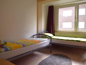 Een studentenkamer met twee eenpersoonsbedden, een raam met gordijnen en een radiator.