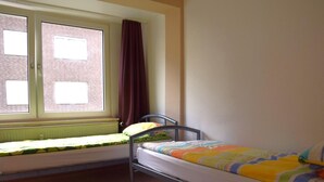 Ein Schlafsaalzimmer mit zwei Einzelbetten, einem Fenster mit Vorhängen, einer Heizung und einem grauen Teppichboden.