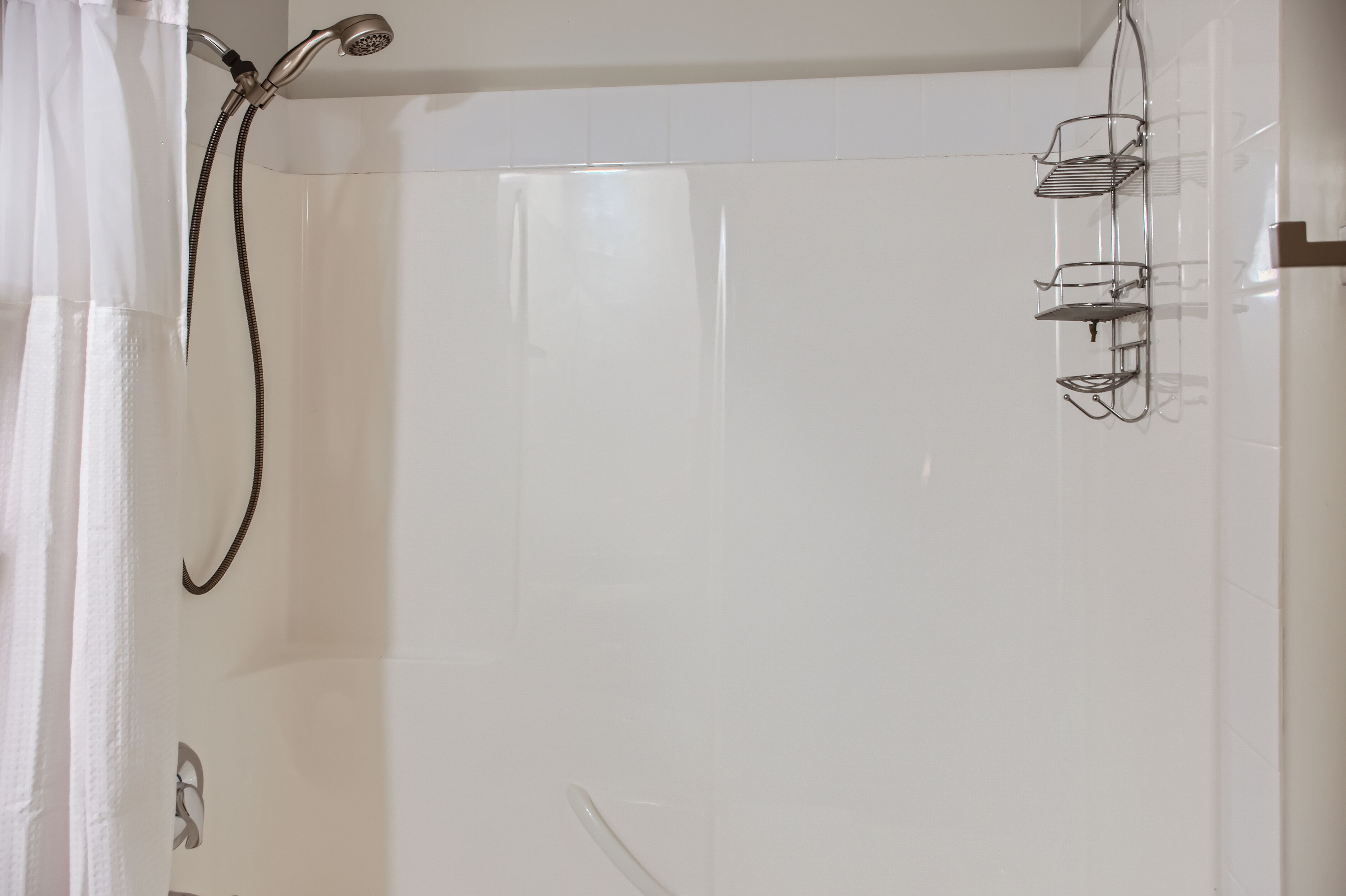 A shower area with a glass door, a showerhead, and a metal shelf.