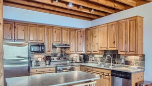 A kitchen with wooden cabinets, stainless steel appliances, and a stone backsplash. - Snowy Creek by Okanagan Premier (Beaverdell)