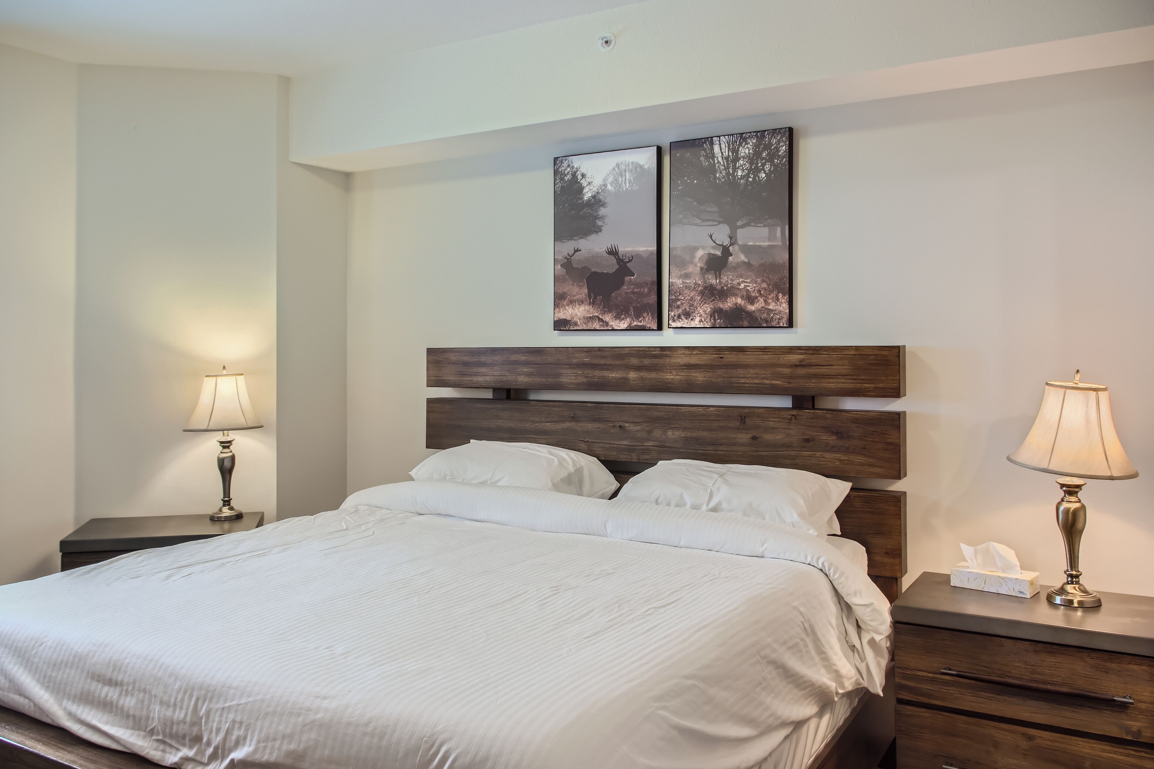 A neatly made bed with white linens, a wooden headboard, and two bedside tables with lamps.