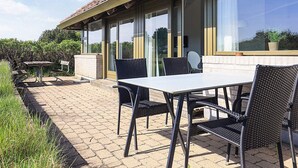 Un patio exterior con una mesa y sillas, un sendero de ladrillos y un edificio con ventanas grandes y techo de tejas.