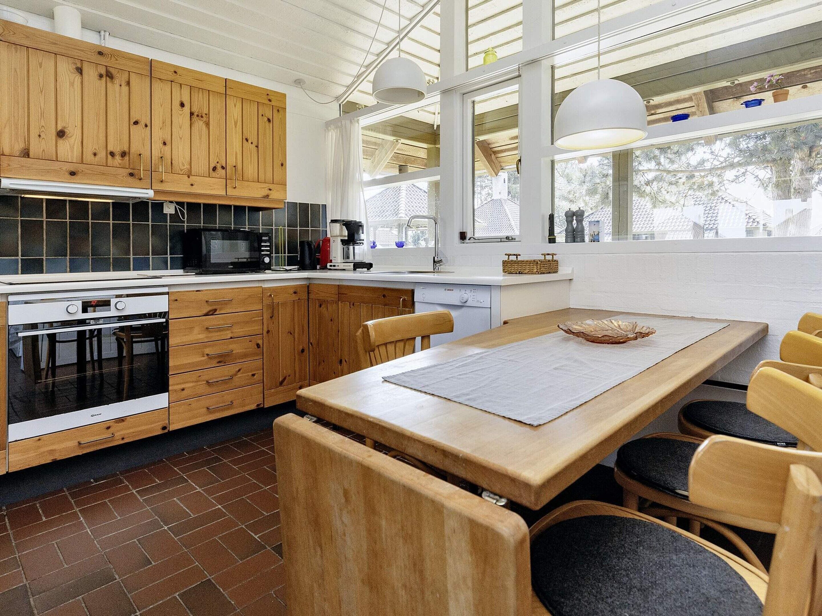 A modern kitchen with wooden cabinets, a built-in oven, and a dining area with a large table and chairs.