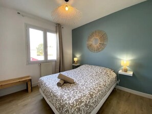 A bedroom with a bed, two bedside tables, a bench, a window, and a wall decoration.