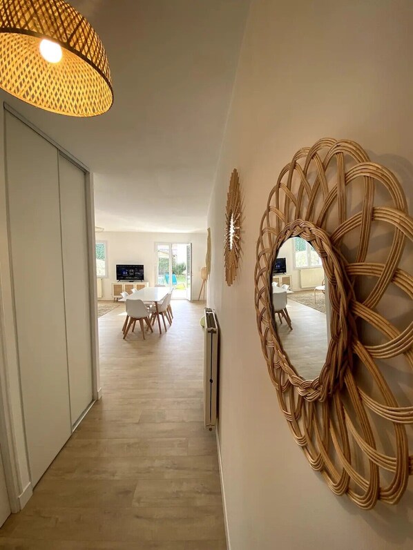 A modern interior with a dining area, a large woven mirror, and a ceiling light fixture.