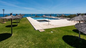 Une piscine avec vue sur la mer, entourée de pelouse et agrémentée de parasols en chaume.