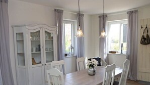 A dining area with a wooden table, white chairs, a glass cabinet, and two pendant lights. - Northern Lights Modern Retreat (Steinberg)