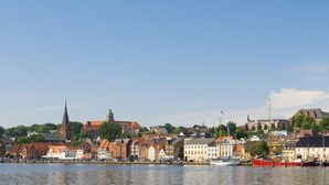 A waterfront cityscape with historic buildings, a prominent church spire, and boats docked along the harbor. - Northern Lights Modern Retreat (Steinberg)