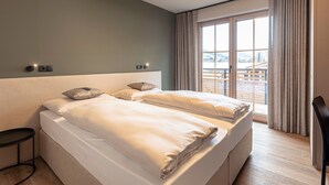 Une chambre d’hôtel moderne avec un grand lit, une table de chevet et une vue sur un paysage enneigé par la fenêtre.
