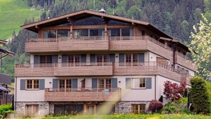 Un immeuble à plusieurs étages, doté de balcons, situé dans une région montagneuse, avec un champ de fleurs jaunes au premier plan.