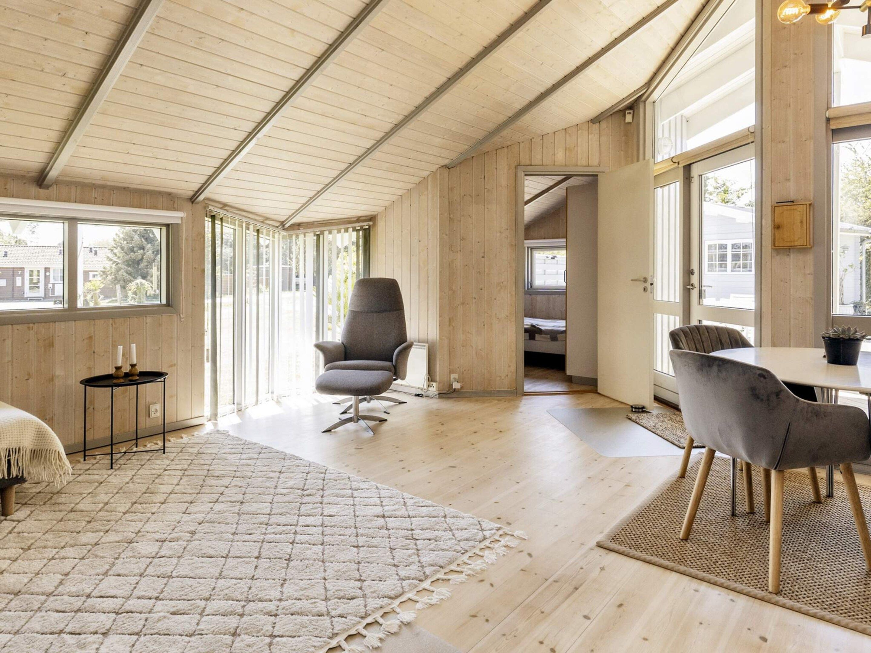 Una habitación amplia con techo alto, paredes de madera, un ventanal grande, una mesa de comedor con sillas, un sofá y una mesita auxiliar.