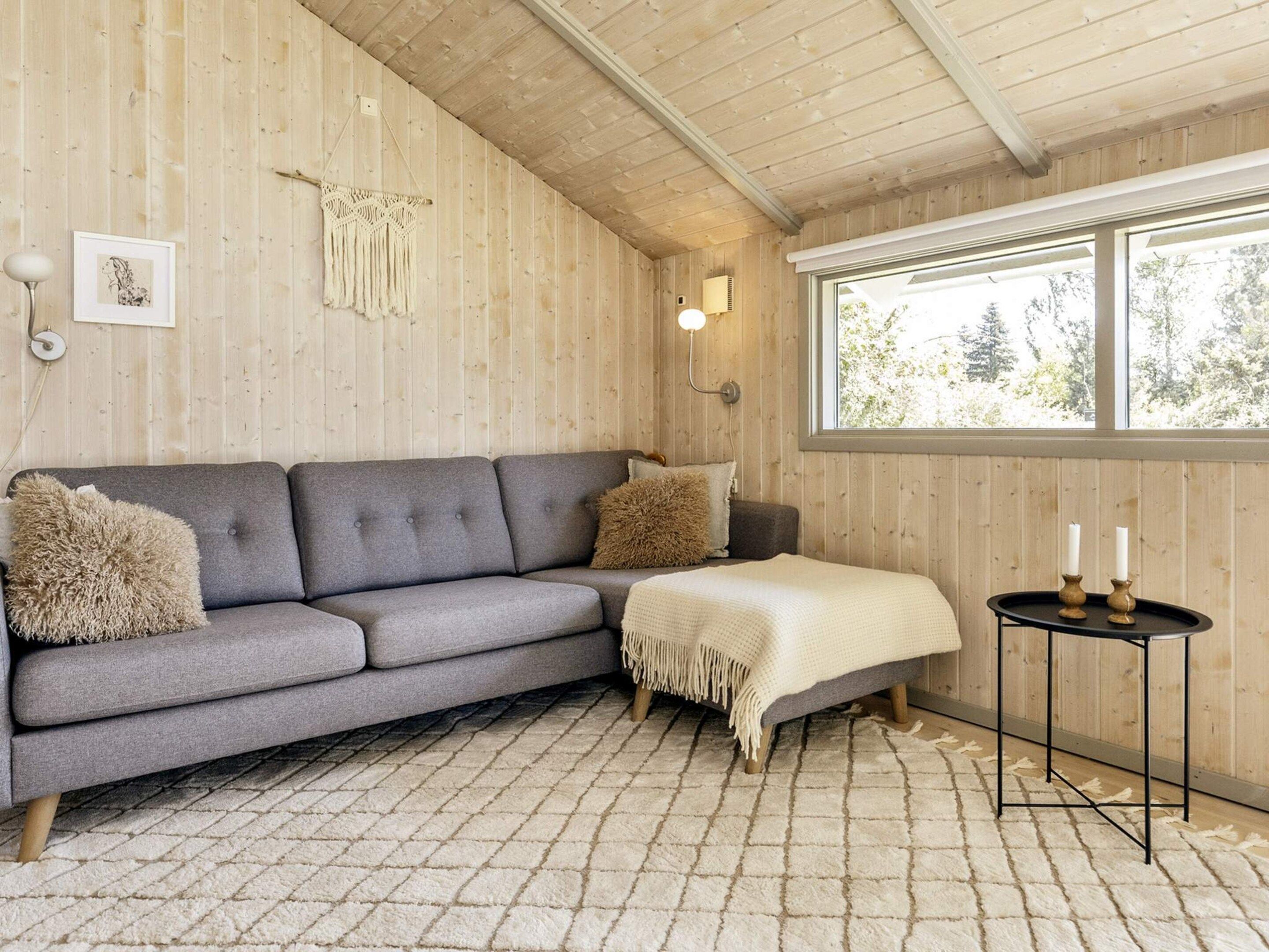 Een gezellige kamer met een grijze bank, een tafeltje met kaarsen en een raam met uitzicht op bomen.