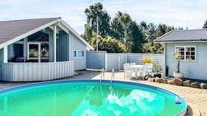En trädgård med en pool, en täckt uteplats och ett inhägnat område med ett litet förråd.