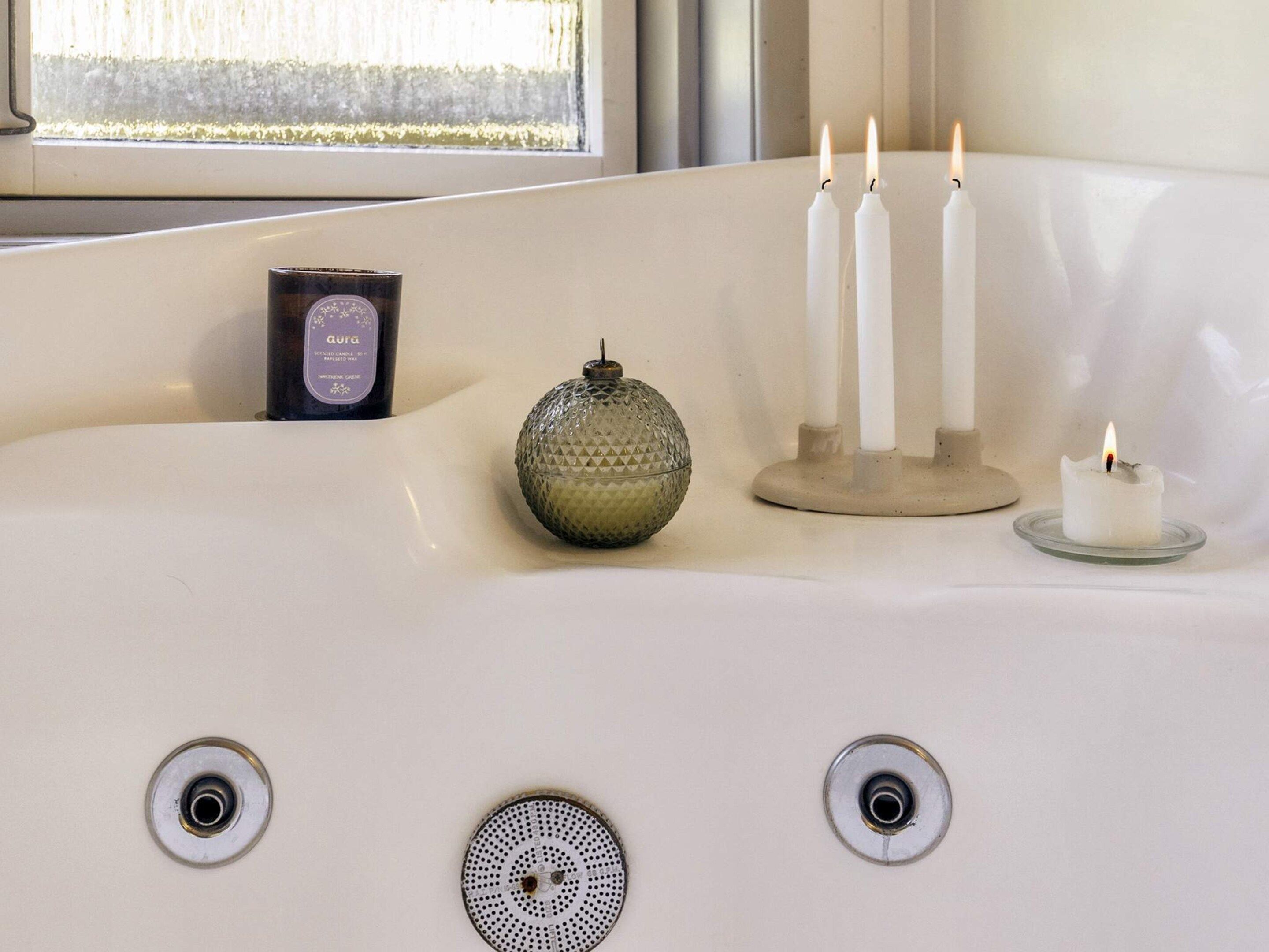 A bathtub with three lit candles, a glass candle holder, and a bottle of candle wax.
