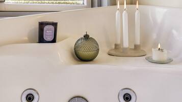 A bathtub with three lit candles, a glass candle holder, and a bottle of candle wax.