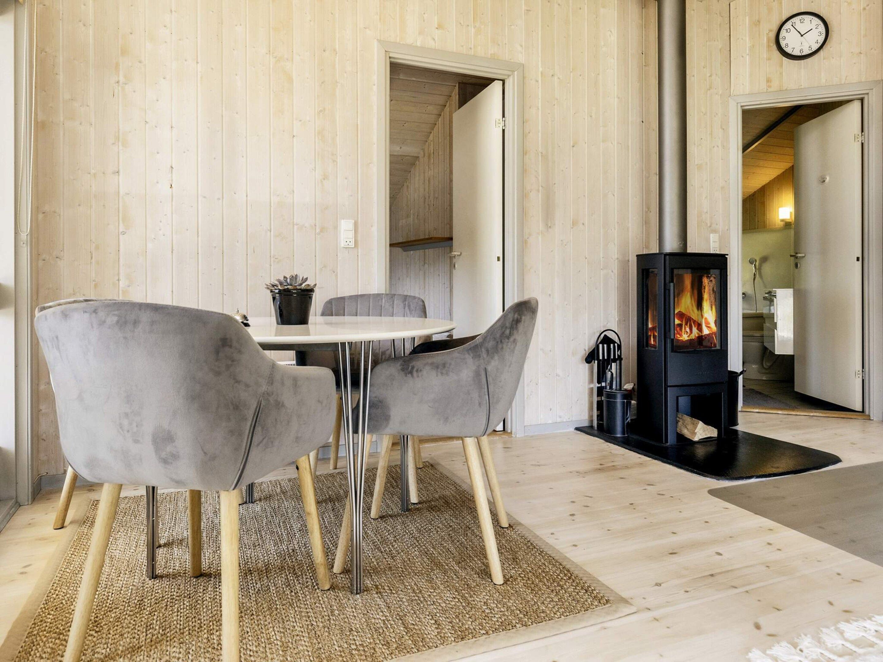 Een modern interieur met een houten wand, een ronde tafel met stoelen, een open haard en een klok.