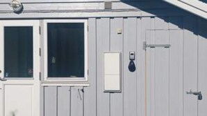 En byggnad med en vit fasad, en dörr med ett fönster och en liten elcentral.