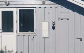 Een gebouw met een witte gevel, een deur met een raam en een klein stroomkastje.