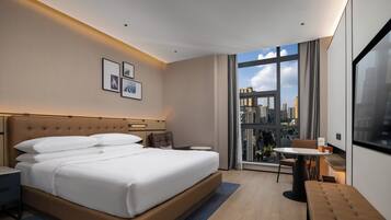 Et moderne hotelværelse med en stor seng, et skrivebord, en stol og udsigt over byen.
