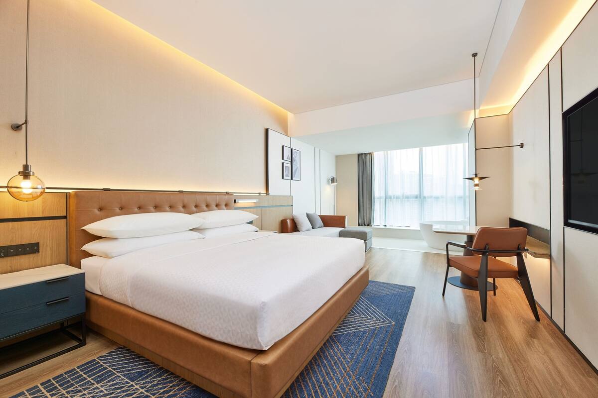A modern hotel room with a large bed, a desk, a chair, and a TV.