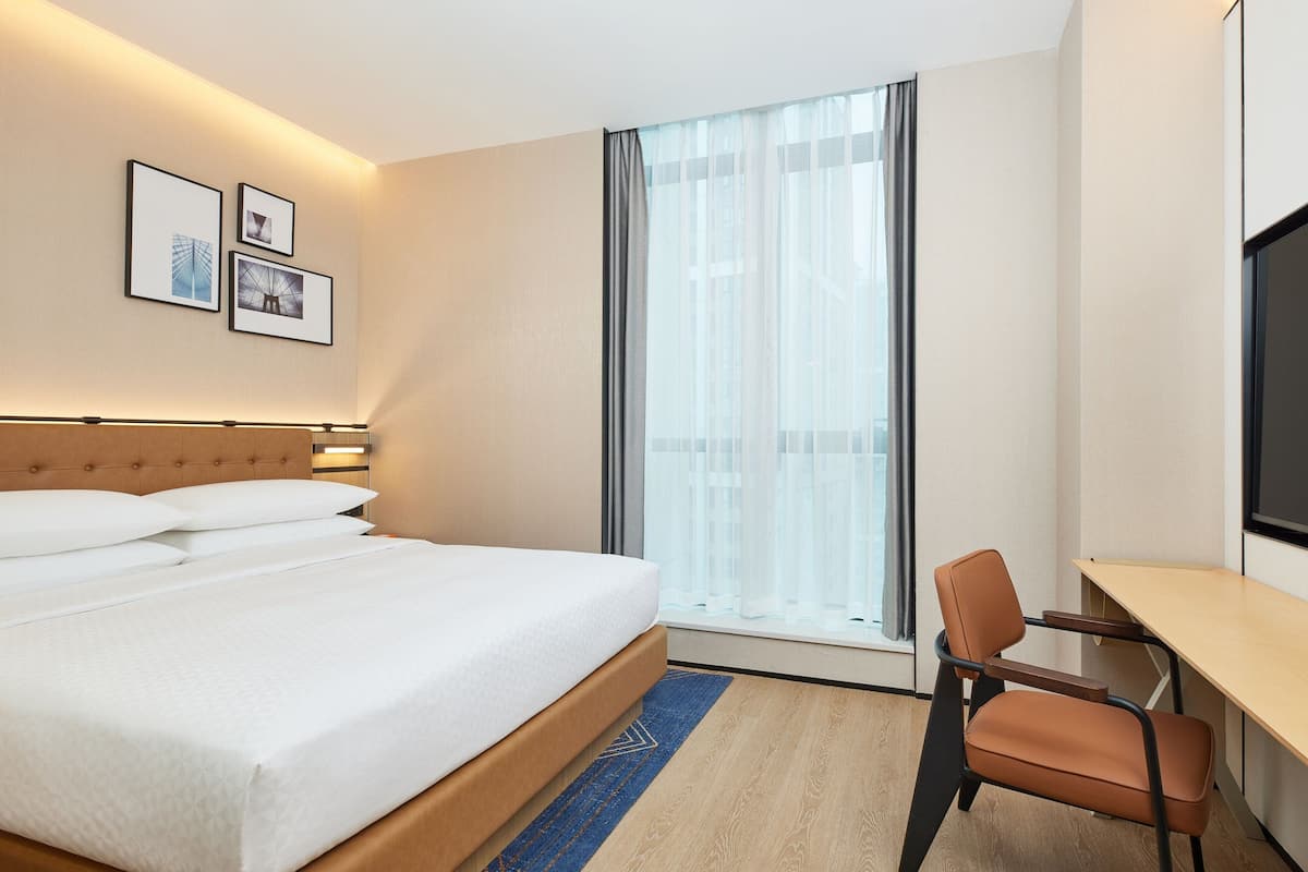 A hotel room with a bed, a desk, and a window with sheer curtains.