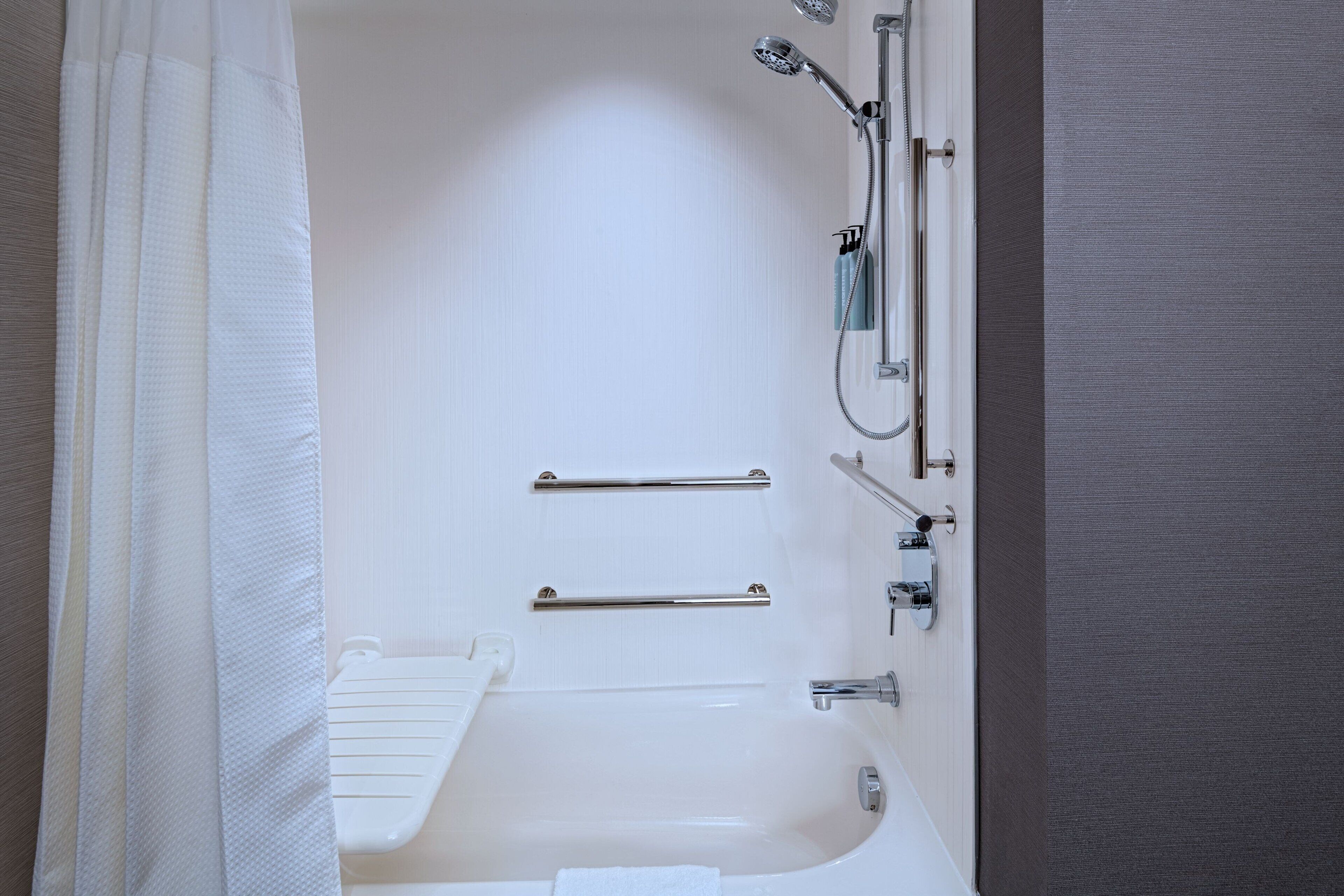 A modern bathroom with a bathtub, shower, and handrails.