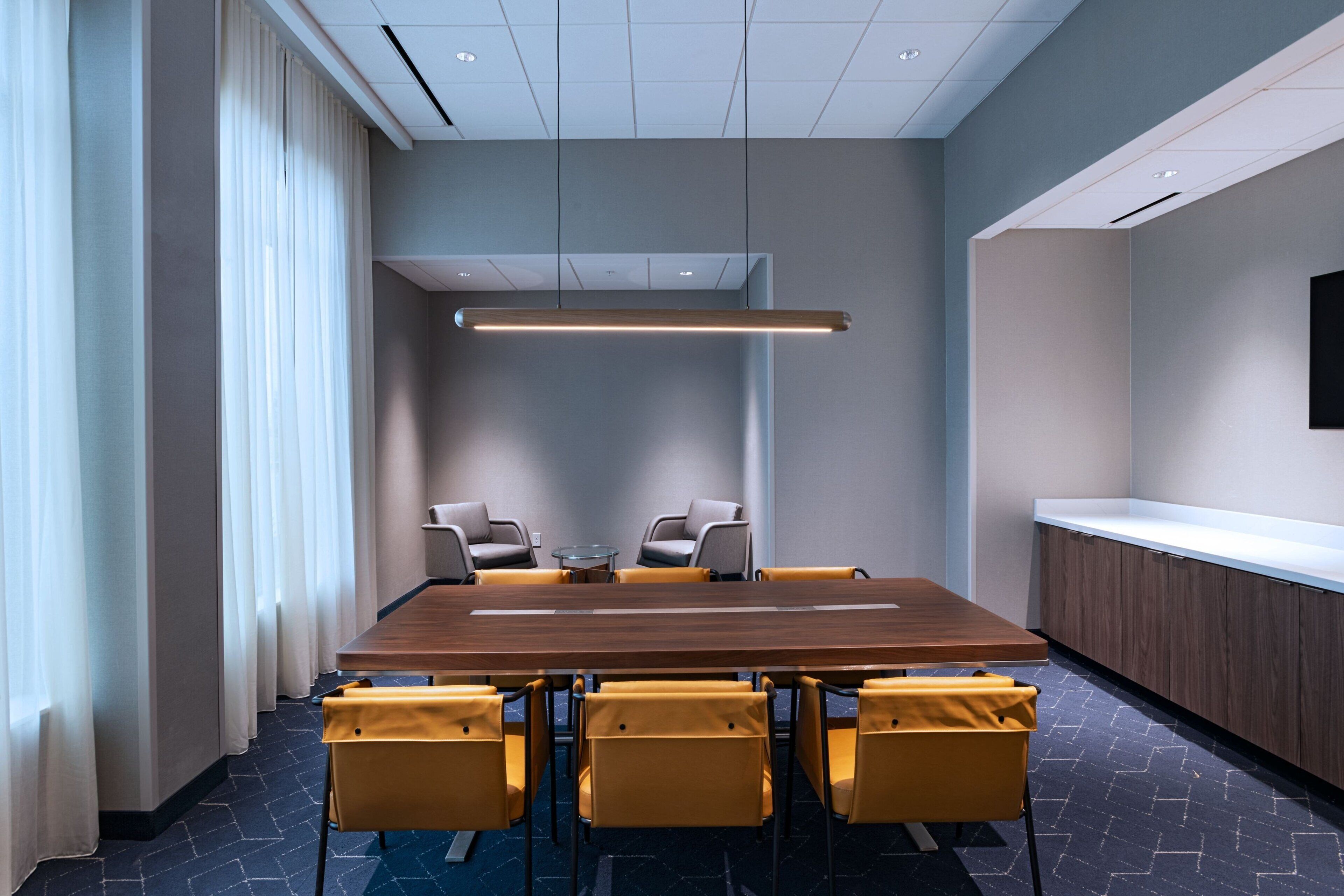 Een vergaderruimte met een lange tafel, gele stoelen en een moderne plafondlamp.