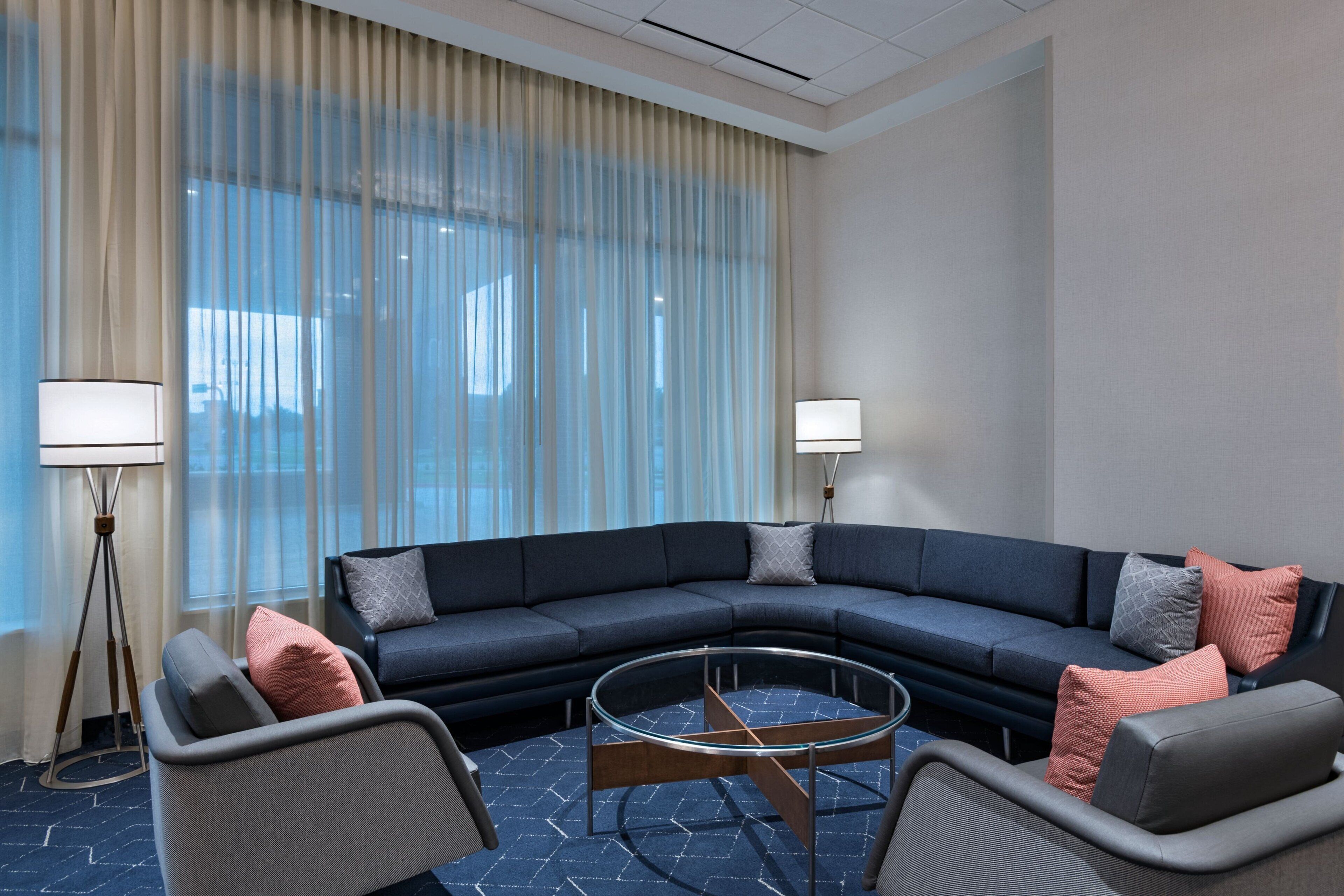 A modern living room with a sectional sofa, two armchairs, a glass coffee table, and a floor lamp.