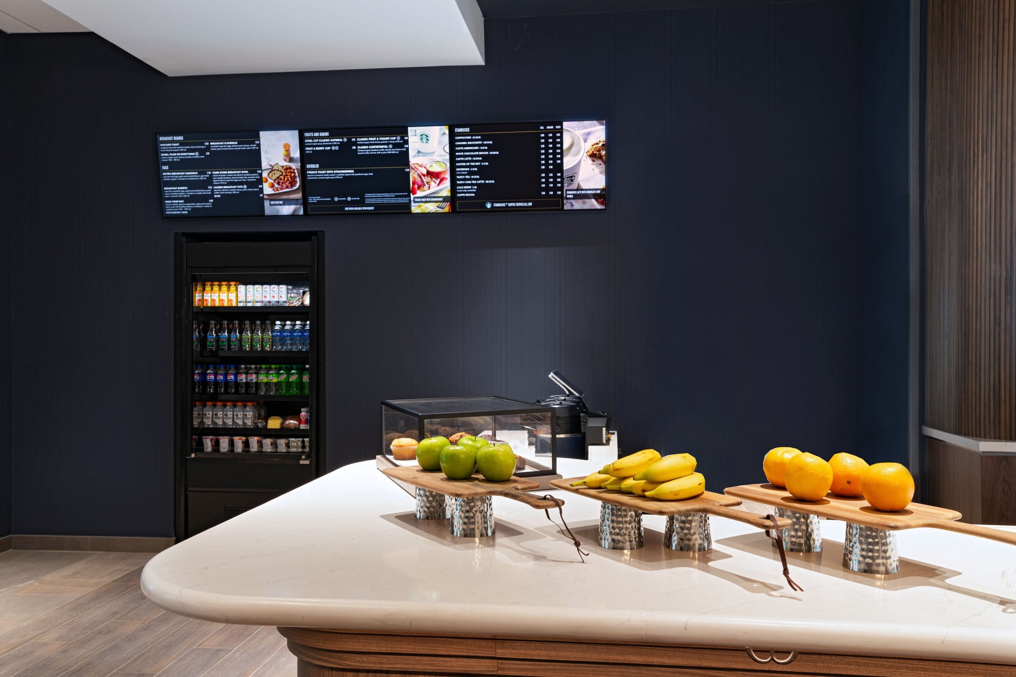 Uma área de bar moderna com um painel de menu, um dispensador de bebidas e expositores de frutas.