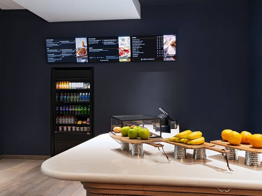 Uma área de bar moderna com um painel de menu, um dispensador de bebidas e expositores de frutas.
