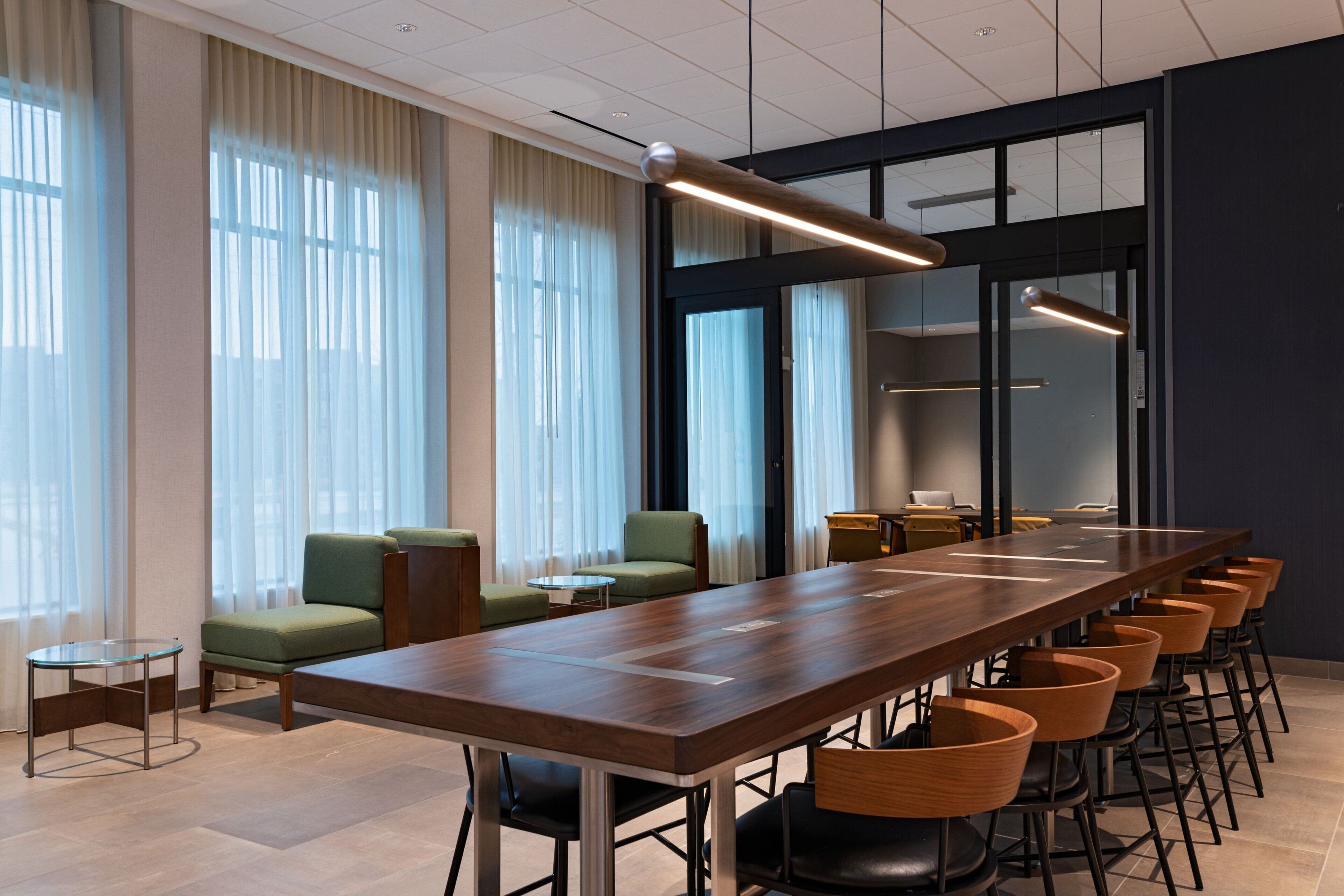 A modern conference room with a long wooden table, multiple chairs, and a glass partition.