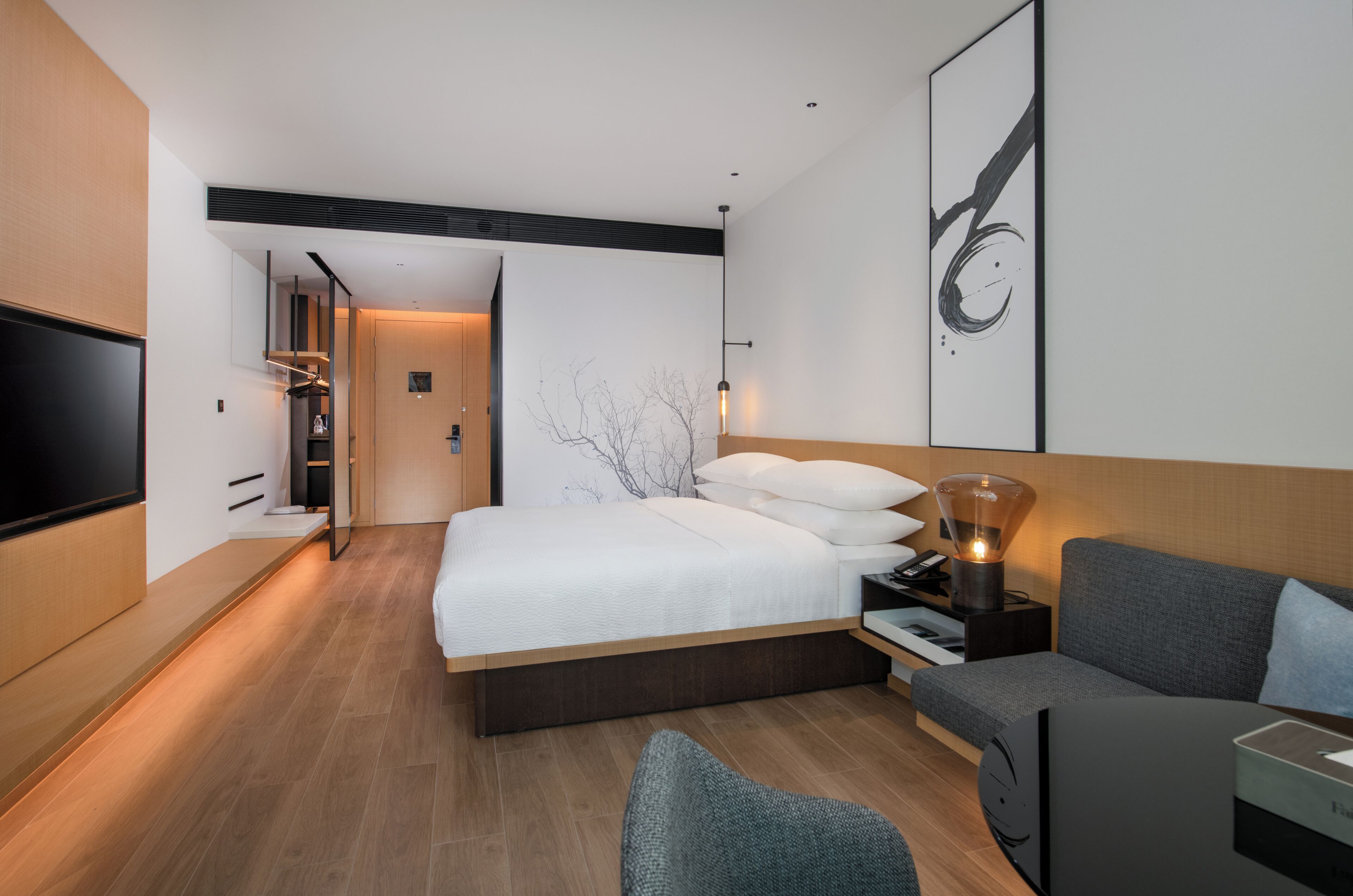 Et moderne hotelværelse med en stor seng, et fjernsyn, et skrivebord med lampe og en sofa.